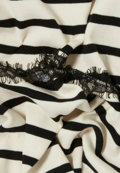 Tessuto a righe crema e nero, caratterizzato da una morbida texture a maglia e un dettaglio in pizzo nero al centro con bordi sfrangiati.