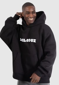Black hoodie made of soft fabric, featuring a front pocket, ribbed cuffs, and a white logo on the chest. Relaxed fit with a large hood.