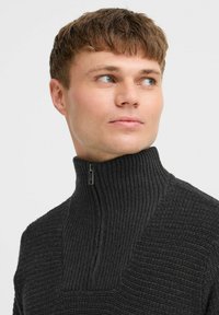 Dunkelgrauer Strickpullover mit hohem geripptem Kragen und halbem Reißverschluss. Die Textur weist horizontale Rippungen und eine taillierte Passform auf.