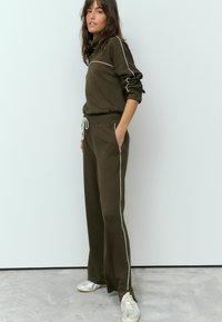 Olive green sweatshirt and matching pants with white side stripes, featuring a drawstring waist and ribbed cuffs, made from soft material.