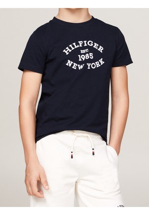 Granatowy bawełniany t-shirt z krótkimi rękawami, ozdobiony białym napisem: "HILFIGER EST. 1985 NEW YORK" w zakrzywionym kształcie na wysokości klatki piersiowej.