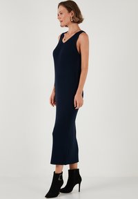 Abito in maglia a coste blu navy con scollatura a V e senza maniche, che arriva a metà polpaccio. Abbinato a stivaletti neri con tacco a spillo.