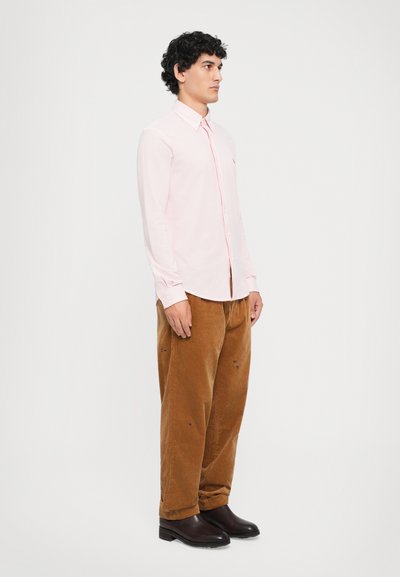 Cămașă lungă roz deschis cu guler cu nasture, asortată cu pantaloni din corduroy maro și cizme maro închise. Design simplu, drept.