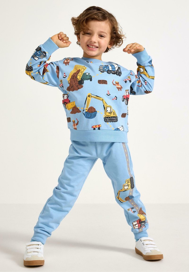 Lichtblauwe sweatshirt en bijpassende broek met patroon van bouwvoertuigen in levendige kleuren. Zachte textuur, elastische manchetten en tailleband.