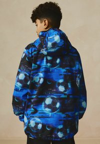 Giacca con cappuccio caratterizzata da un vivace design blu con palloni da calcio grafici e motivi astratti. Realizzata in materiale leggero e morbido.
