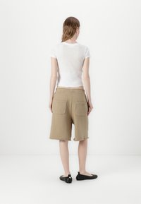 Biała dopasowana koszulka z krótkim rękawem w połączeniu z beżowymi, szortami do kolan z postrzępionym wykończeniem i dwiema tylnymi kieszeniami. Czarne buty typu slip-on dopełniają całość.