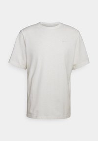 Camiseta de manga corta y cuello redondo en beige claro, hecha de una tela suave, con un pequeño logo de Nike en el pecho. Corte casual con dobladillo recto.