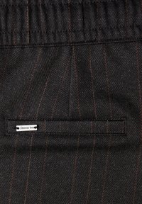 Zwarte stof met oranje pinstripes, voorzien van een elastische tailleband en een klein, zilverkleurig labeltje dichtgenaaid bij een achterzak.