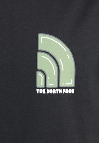 Grøn stiliseret kvart cirkel-logo med hvide accenter over "THE NORTH FACE" teksten på sort stofbaggrund.