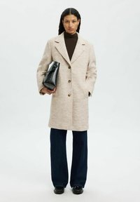 Beige Wollmischungmantel mit Reverskragen, drei Knöpfen und Seitentaschen, kombiniert mit dunklen Denim-Hosen und einer schwarzen Handtasche.
