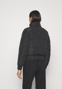 Czarna kurtka puchowa z wysokim kołnierzem, rombowym pikowaniem, elastycznymi mankietami oraz krótkim krojem. Tekstura jest gładka i błyszcząca.