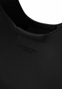 Zwarte leren tas met een gestructureerd oppervlak. Heeft een ronde opening en een verwerkt merkembleem. Eenvoudig ontwerp met minimale hardware.