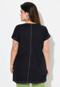 Túnica negra de manga corta, con escote redondo y costuras con hilo plateado. El material parece suave, con un corte holgado y un ligero brillo.