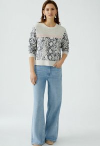 Leichter Pullover mit Schlangendruckdesign in Grau und Schwarz, mit einem einfarbigen rosa Streifen an der Oberseite; kombiniert mit weit geschnittenen blauen Jeans.