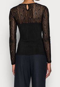Top nero con lunghe maniche in pizzo con motivo floreale, corpo aderente, dettaglio a goccia sulla schiena e texture a coste nella parte inferiore.
