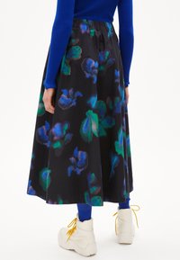 Jupe noire avec un motif floral dans des nuances de bleu et de vert, dotée d'une taille élastique et d'un design fluide. Associée à des chaussures blanches.