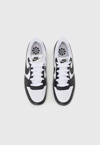 Hvide og sorte Nike sneakers med en glat læder- og mesh-overdel, der har perforeringer, flade hvide snørebånd og et Nike-logo på tungen.