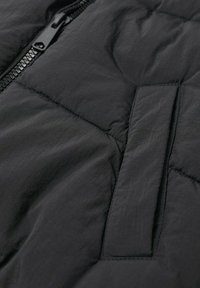 Czarna kurtka puchowa z detalami, w tym pikowaną strukturą, gładką fakturą, zamek błyskawiczny z przodu oraz kieszenią na klapę po lewej stronie.