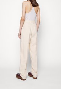 Krämfärgade vida byxor i mjukt tyg, med hög midja och en enda bakficka. Kompletterar bruna skor.