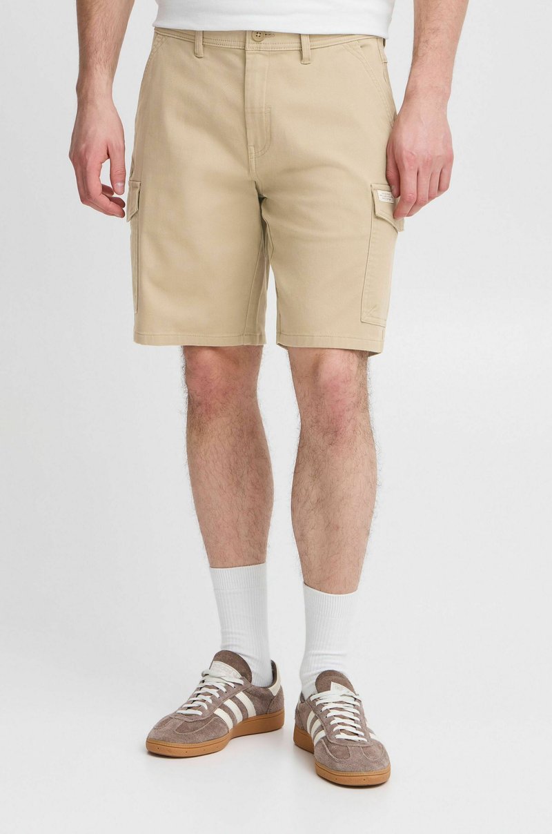 Beige cargo shorts laget av en bomullsmiks, med sidelommer og en avslappet passform. Brukt med hvite sokker og brune semskede sneakers.