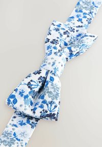 Bomullsskjortslips i vitt med blått och mörkblått blommönster. Har en texturerad yta och formad för en klassisk fluga.