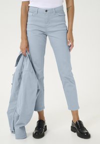 Jean bleu clair au design ajusté, taille haute, cinq poches et une longueur légèrement cropped, associé à une veste assortie et des mocassins noirs.