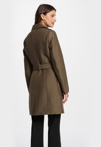 Olijfgroen trenchcoat met een taillering, lange mouwen, omgeslagen kraag en zijzakken; gladde textuur en nauwkeurige naden.