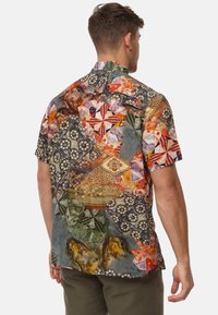 Camisa de manga corta con un diseño de patchwork multicolor que presenta motivos florales, geométricos y de animales sobre un fondo oscuro.