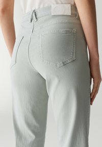 Jeans in denim grigio chiaro con tasche posteriori e un'etichetta bianca sul cinturino. Il tessuto ha una texture liscia e leggermente lucida.