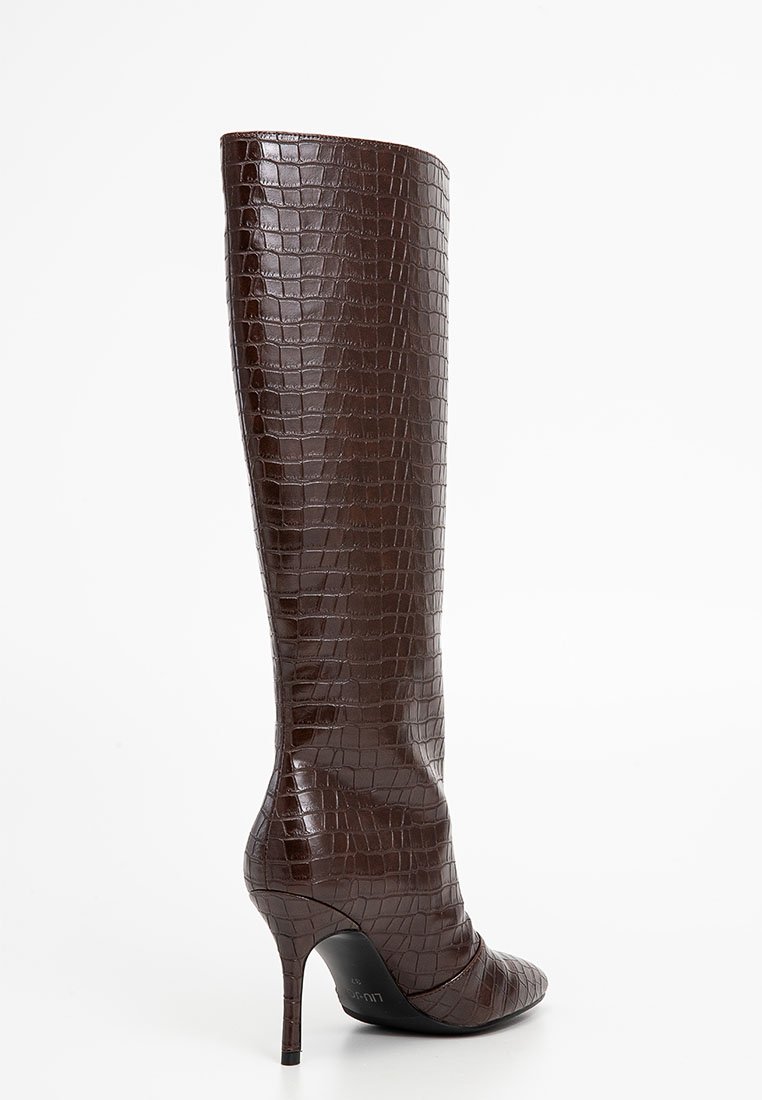 Stivale in pelle marrone con embossing a forma di coccodrillo, altezza ginocchio, punta affilata e tacco a stiletto. Texture liscia e design elegante.