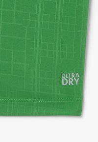 Camiseta atlética verde con un diseño texturizado, etiqueta "ULTRA DRY" en blanco y forma ajustada con tela acanalada.