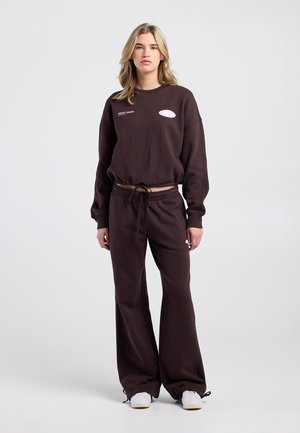 Bruine, loszittende trui met lange mouwen en geribbelde manchetten, geborduurd logo. Bijpassende bruine sweatpants met brede pijpen en trekkoord in de taille.