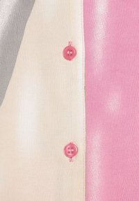 Chemise à boutons en tissu rose, gris et crème. Comprend des boutons roses et des surpiqûres contrastées. Texture lisse avec une légère brillance.