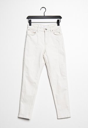 Jean en denim blanc avec une coupe slim, design à cinq poches, fermeture éclair et passants de ceinture. Suspendu à un cintre noir en plastique sur un fond blanc.