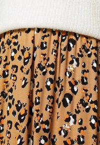 Pull en maille blanche associé à une jupe plissée avec un motif léopard beige, noir, blanc et orange.
