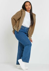 Brun fleece-fodrad jacka med en khaki huva, kombinerad med blå vida jeans och vita sneakers. Enkel vit t-shirt under.