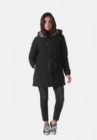 Parka noire isolée avec une doublure de capuche grise, dotée de zips sur les poches et d'une taille légèrement cintrée pour un ajustement sur mesure.
