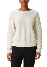 Pull en crème tricoté avec un col large, présentant un motif en zigzag texturé et des poignets et un ourlet côtelés. Associé à un pantalon noir.