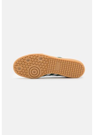 Podeszwa buta Adidas z teksturowanym gumowym chwytem, okrągłymi i falistymi wzorami oraz wytłoczonym logo Adidas na środku.