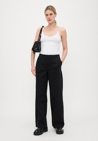 Black wide-leg trousers with front pleats, paired with a white tank top. Accessories include a small black handbag and platform shoes.