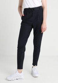 Svarta byxor med pinstripes i lätt tyg, med dragsko i midjan, tapered passform och sidofickor. Bärs med vita sneakers.