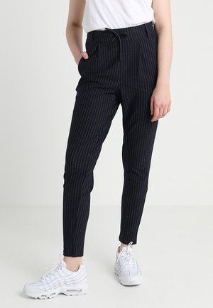 Schwarze, gestreifte Hose aus leichtem Stoff mit Kordelzugbund, schmalem Schnitt und seitlichen Taschen. Getragen mit weißen Sneakers.