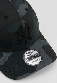 Black camo cap with embroidered "NY" logo, curved brim, six-panel design, adjustable strap, and circular tag with "New Era 9FORTY."