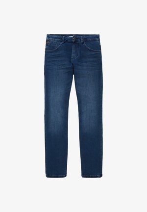 Mężczyzna ubrany w jasnoszary sweter, niebieskie jeansy i białe trampki, stojący na neutralnym tle.