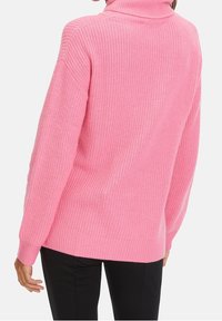 Rosa Strickpullover mit hohem Kragen, gerippter Textur und überschnittenen Schulternähten. Lange Ärmel und entspannte Passform, endet auf Hüfthöhe.