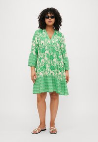 Πράσινο λουλουδάτο φόρεμα με τρία τέταρτα μανίκια, v-λαιμόκοψη και στρωτή βάση. Φτιαγμένο από ελαφρύ ύφασμα με υφή λουλουδάτου μοτίβου.