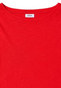 T-shirt rosso realizzato in tessuto morbido e leggero. Caratterizzato da un classico collo a giro e un'etichetta con la scritta "CECIL" vicino al colletto.