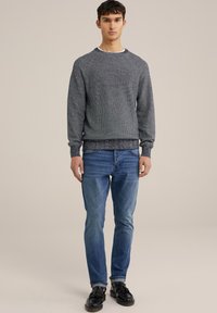 Pelēks teksturēts džemperis ar apaļu izgriezumu, apvienots ar zilām jeans un melnām kurpēm. Džemperim ir ribotas aproces un apakšmalas.