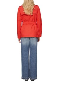 Sarkani jaku ar jostu un apkakli, uzvilkts virs gaiši mazgātiem, platām biksēm. Biksēm ir saplēstas maliņas un kabatas aizmugurē.