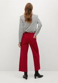 Una camiseta de manga larga a rayas en blanco y azul marino, combinada con pantalones rojos de pierna ancha y cintura alta. Botines negros complementan el atuendo.